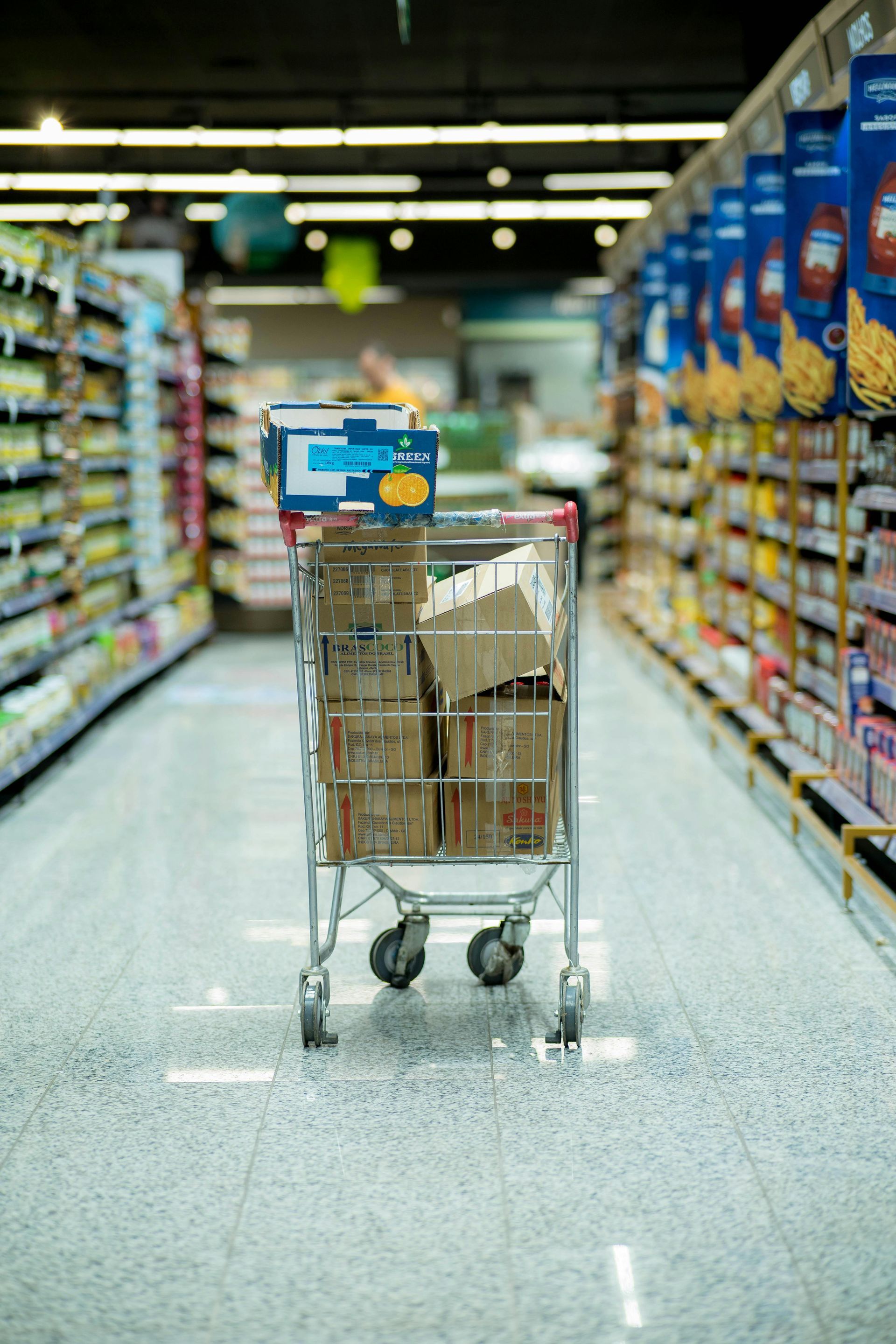 A shopping cart is filled with boxes in an aisle of a supermarket.