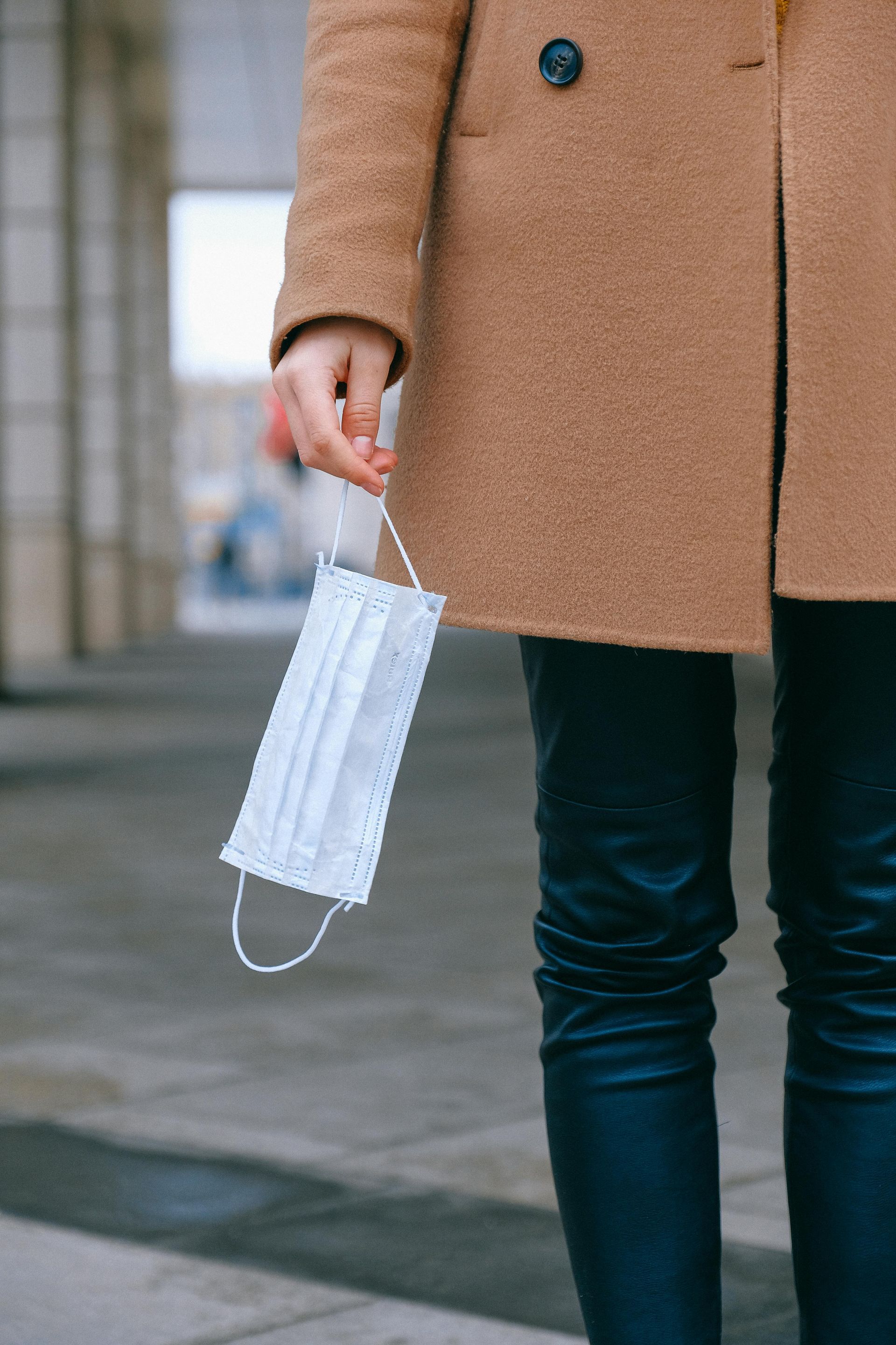 A woman in a coat is holding a medical mask in her hand.