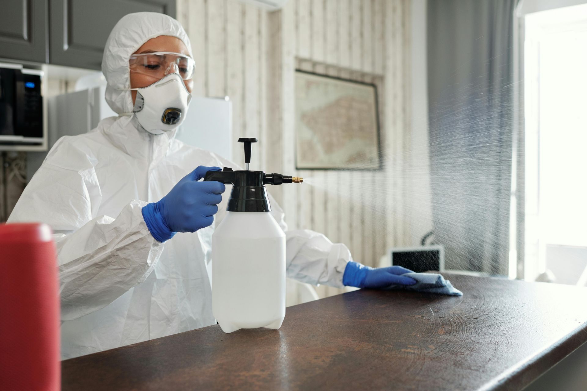 A woman in a protective suit is cleaning a counter in a kitchen.