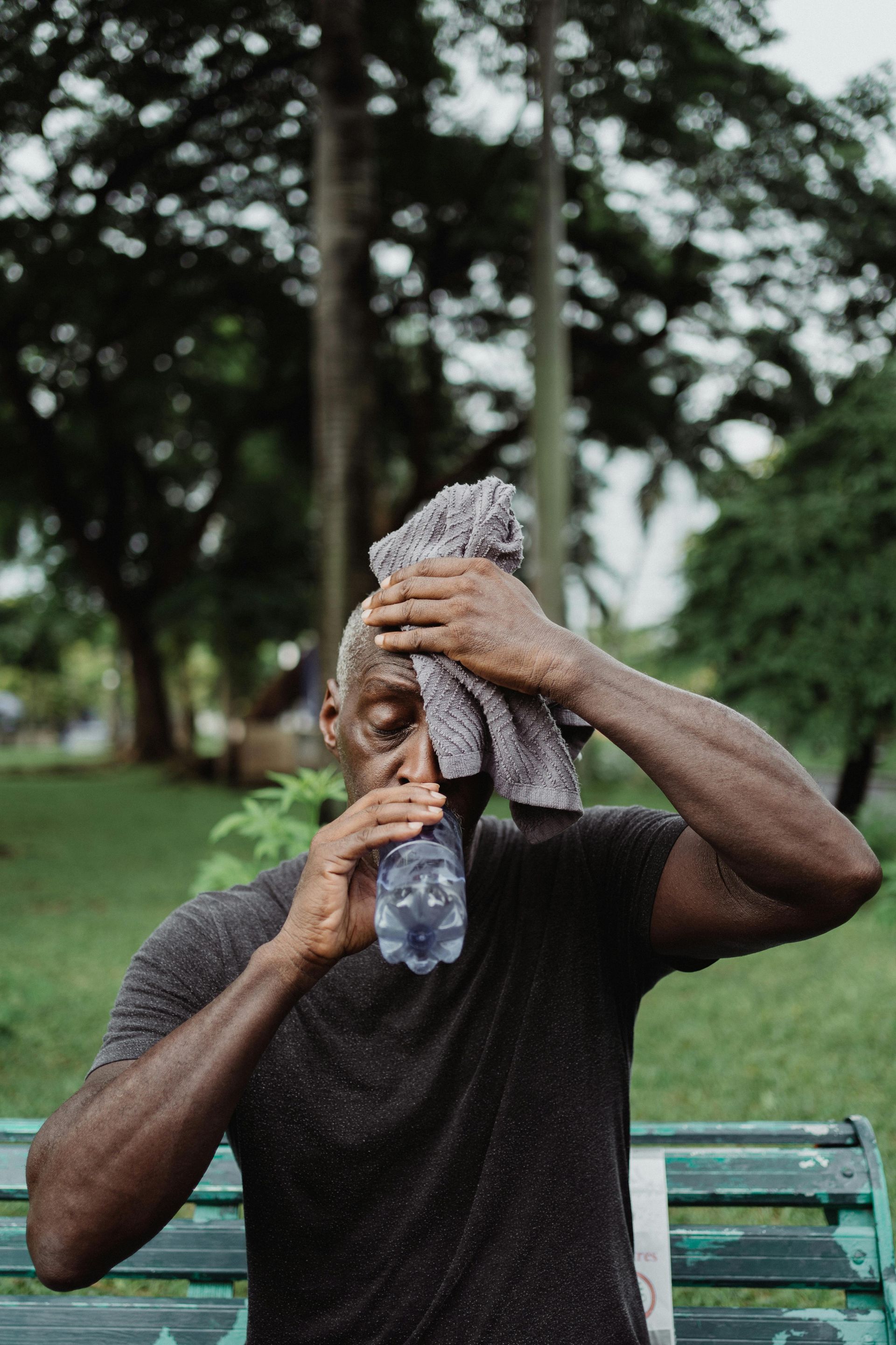 A man is wiping his face with a towel and drinking water from a bottle.