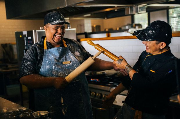 Two men are standing in a kitchen holding rolling pins.