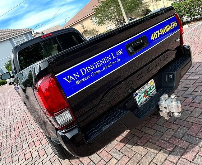 A black truck with a van dingen law sticker on the back is parked on a brick sidewalk.