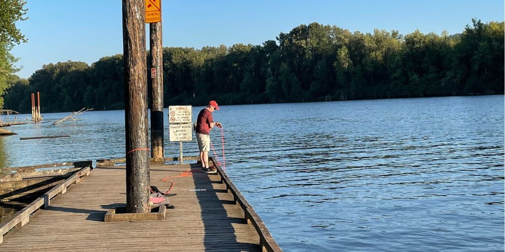 A man is magnet fishing on a dock next to a lake.