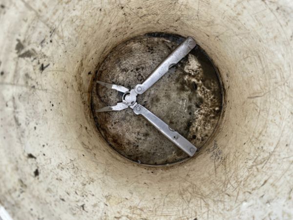 Multi-tool pliers inside a dirty, light-colored bucket.