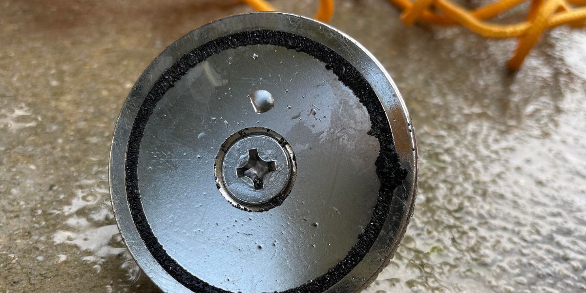 A close up of a metal object with a screw in the middle on a concrete surface.