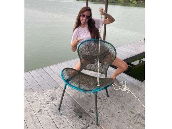 A woman is sitting on a chair on a dock near a lake.