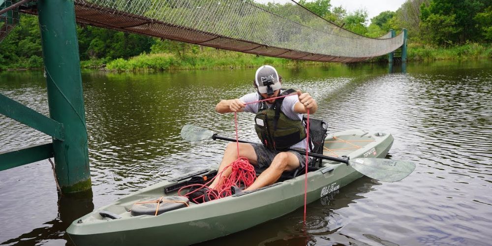 A man is sitting in a kayak on a river under a bridge.