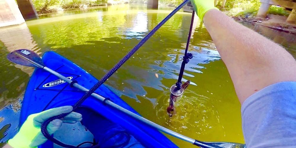 A person is fishing in a blue kayak on a river.