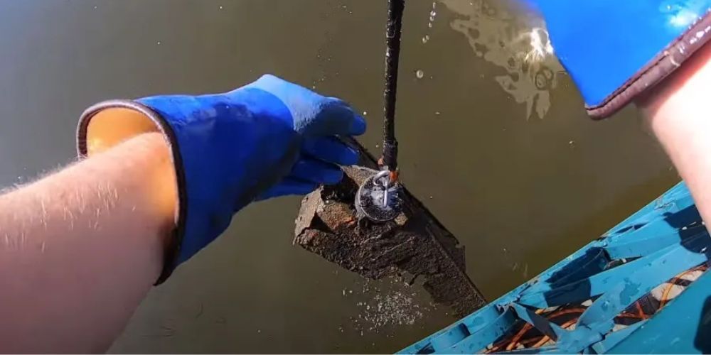 A person wearing blue gloves is holding a piece of metal in the water.