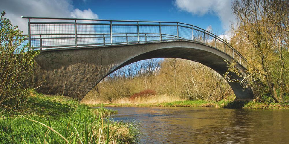 There is a bridge over a river in the middle of a field.