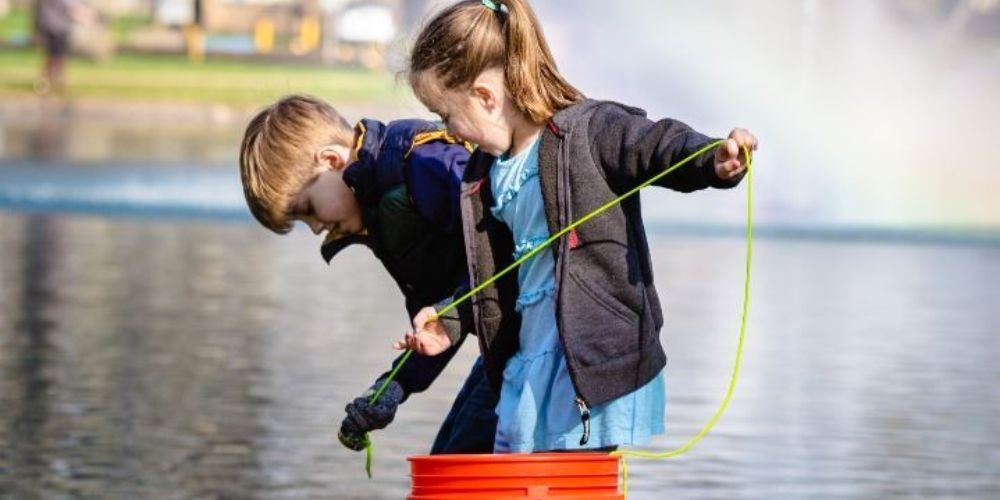 A boy and a girl are standing on top of a red bucket in the water.
