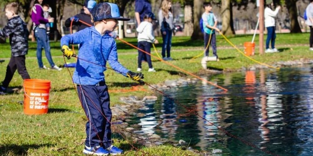 A group of children are fishing in a pond in a park.