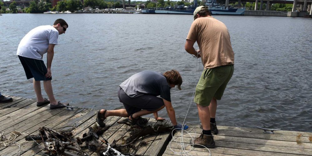 Three men are magnet fishing on a dock near a body of water