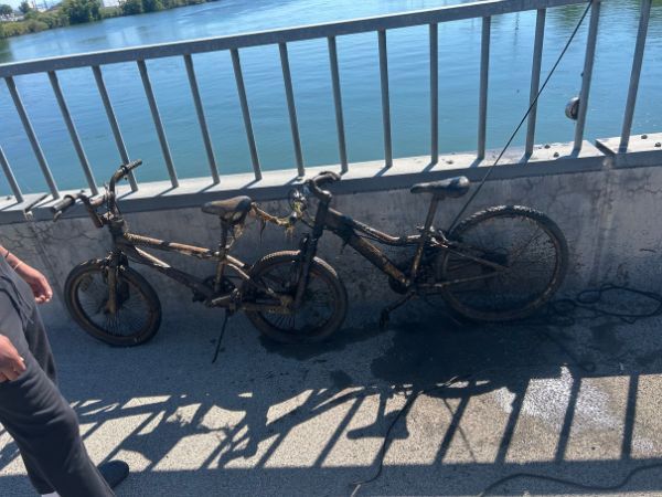 Two muddy bikes recovered from water, resting on a bridge railing near a river.