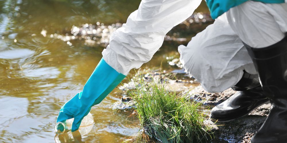 A person wearing blue gloves is taking a sample of water from a river.