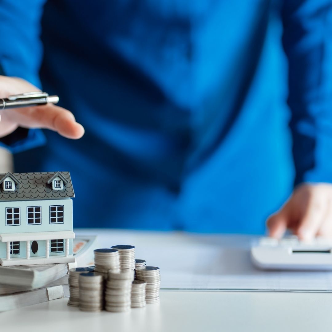 A person is shown with a small model house, stacks of coins, and a calculator, symbolizing property investment and financial management.