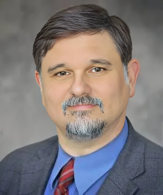 A man with a beard is wearing a blue suit and a blue shirt.