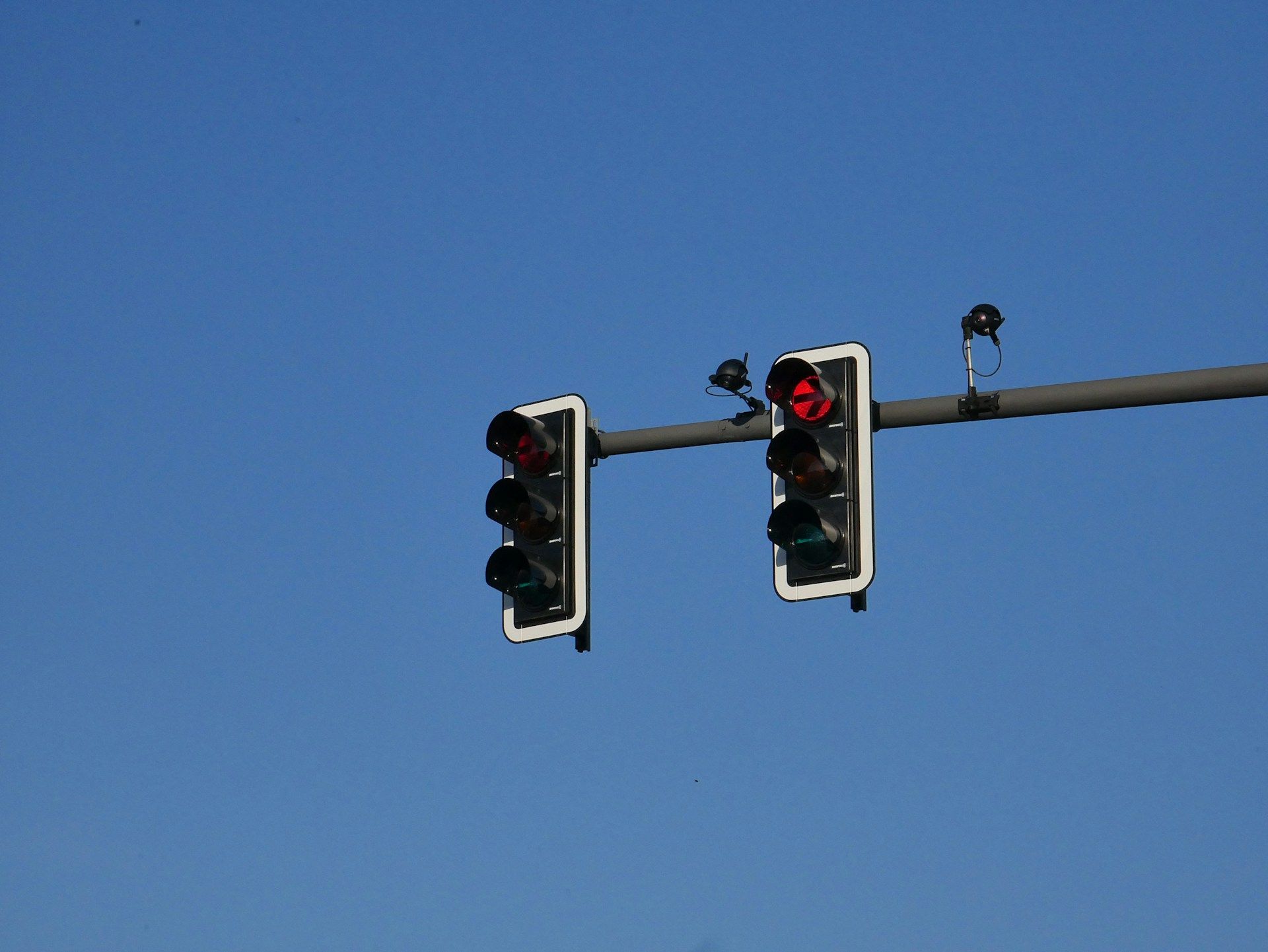Two traffic signals hanging from a bar against a clear blue sky, both displaying a solid red light.