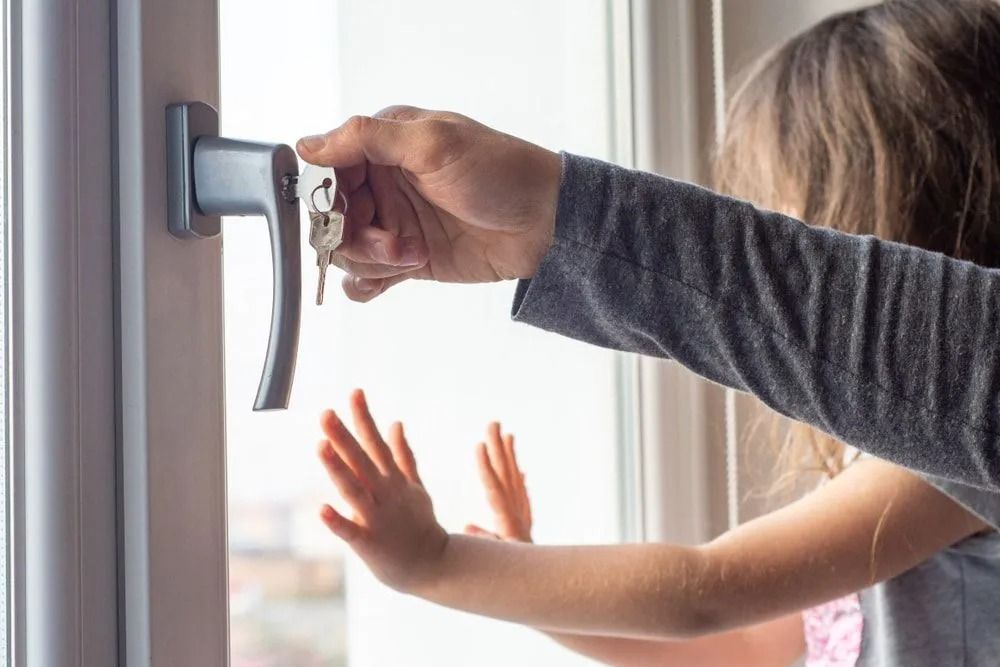 Person with keys opening a window while a child puts hands up to it.