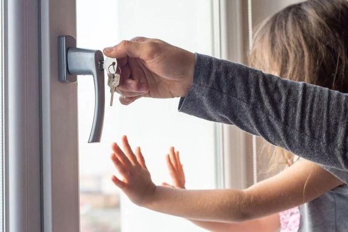 A person using a key to open a window, with a child's hands raised near the glass.