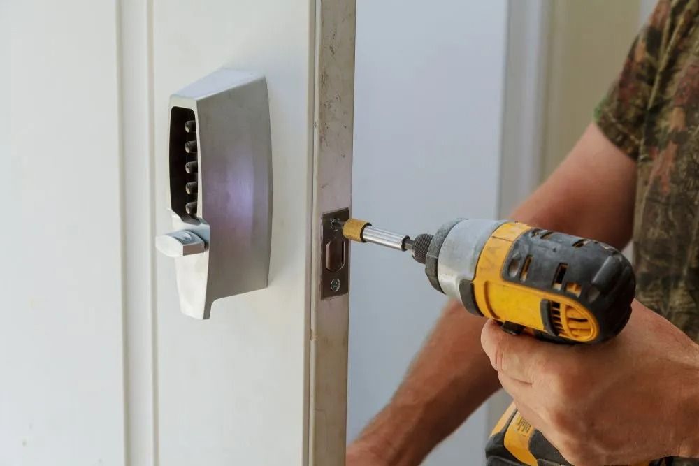 Person using a power drill to install a digital door lock on a white door frame.