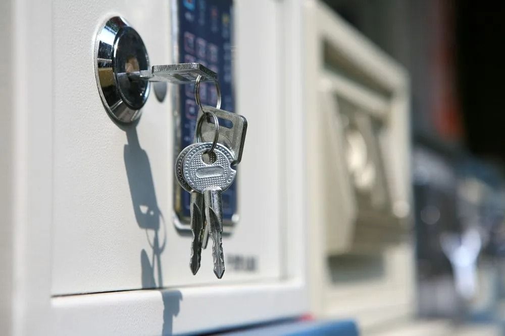 A white safe with keys in the keyhole. Close-up shot, indoors.