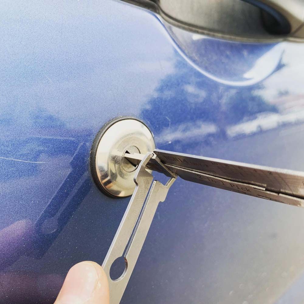 A hand using lock picks on a car door lock, likely attempting to unlock it.