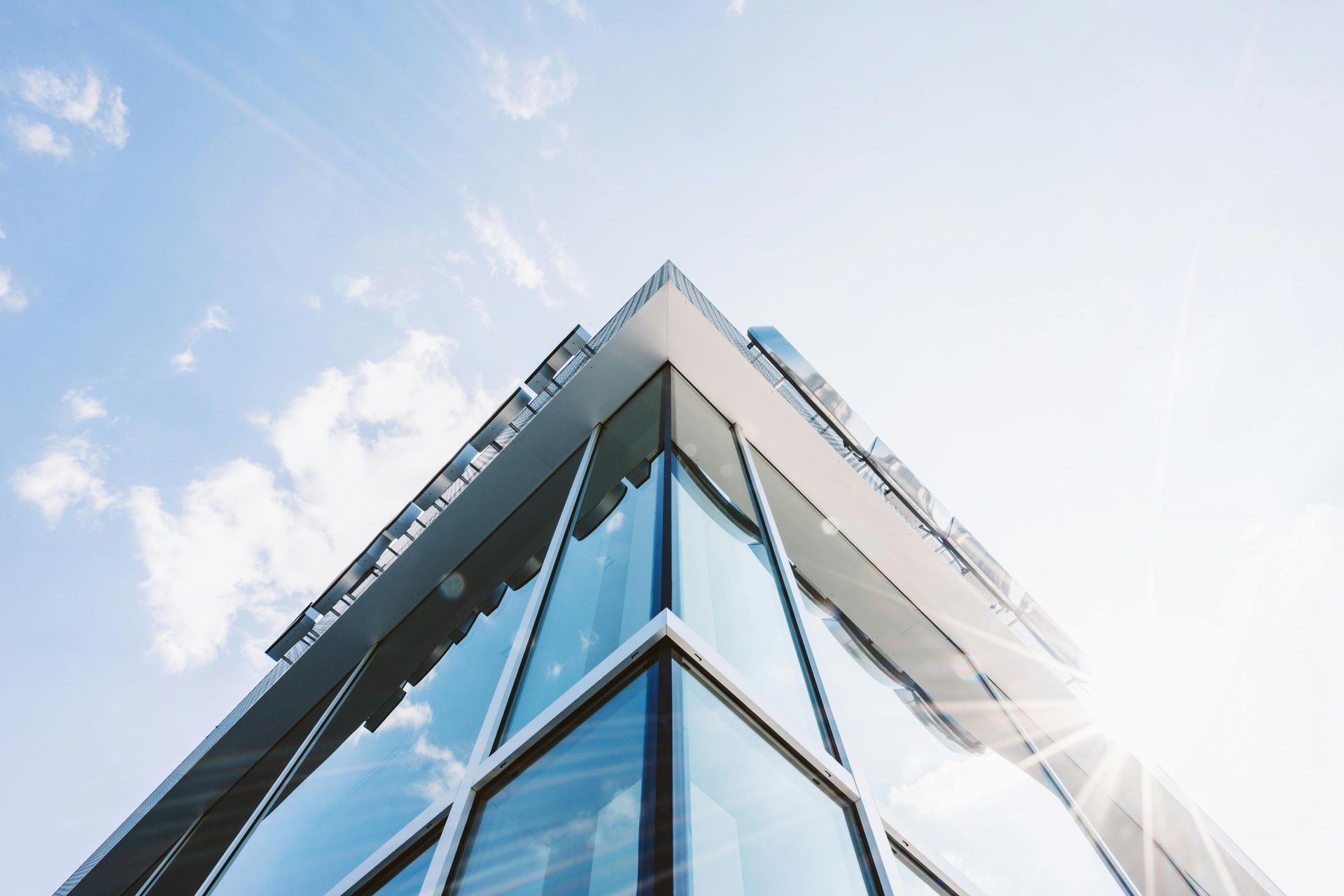 Modern glass building corner against a bright blue sky with sunlight.
