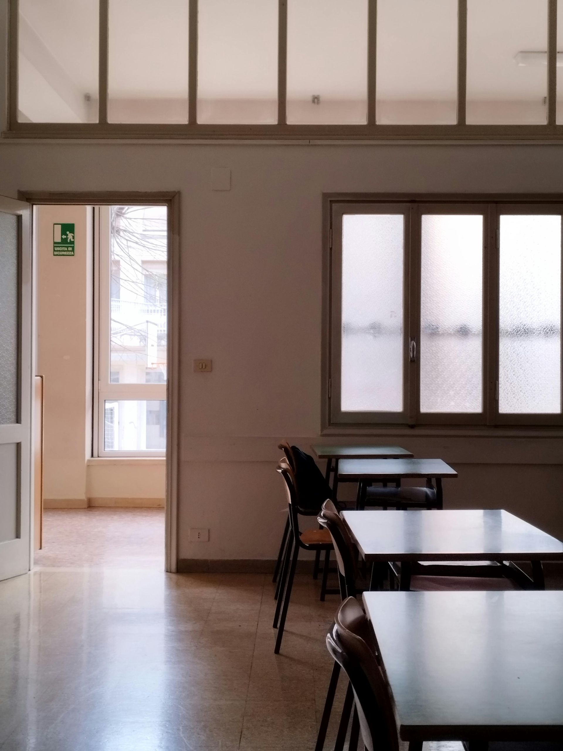 Empty classroom with desks and chairs, natural light through windows and doorway.