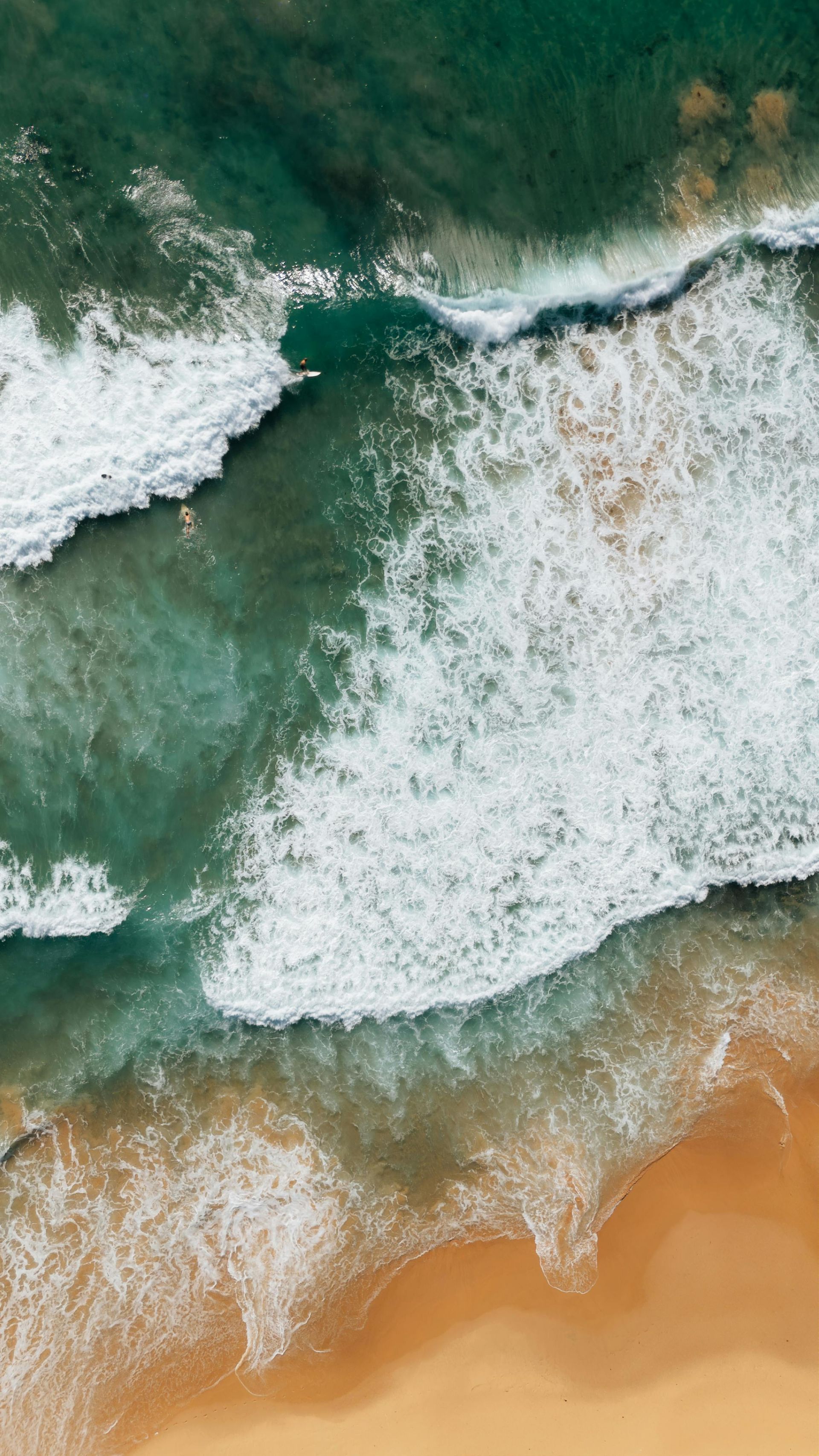 Ocean waves crashing on a sandy beach; turquoise and white water meets golden sand.