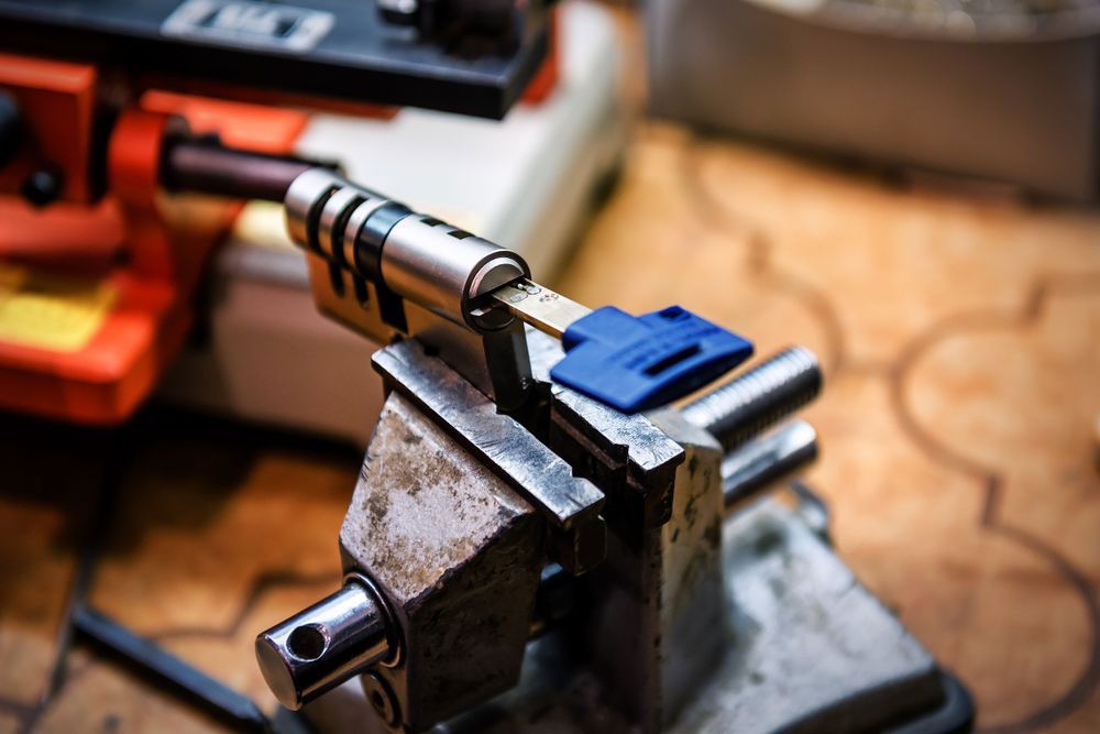 Locksmith cutting a key in a vise. The key is blue, the machine is orange and black, and the setting is a workshop.