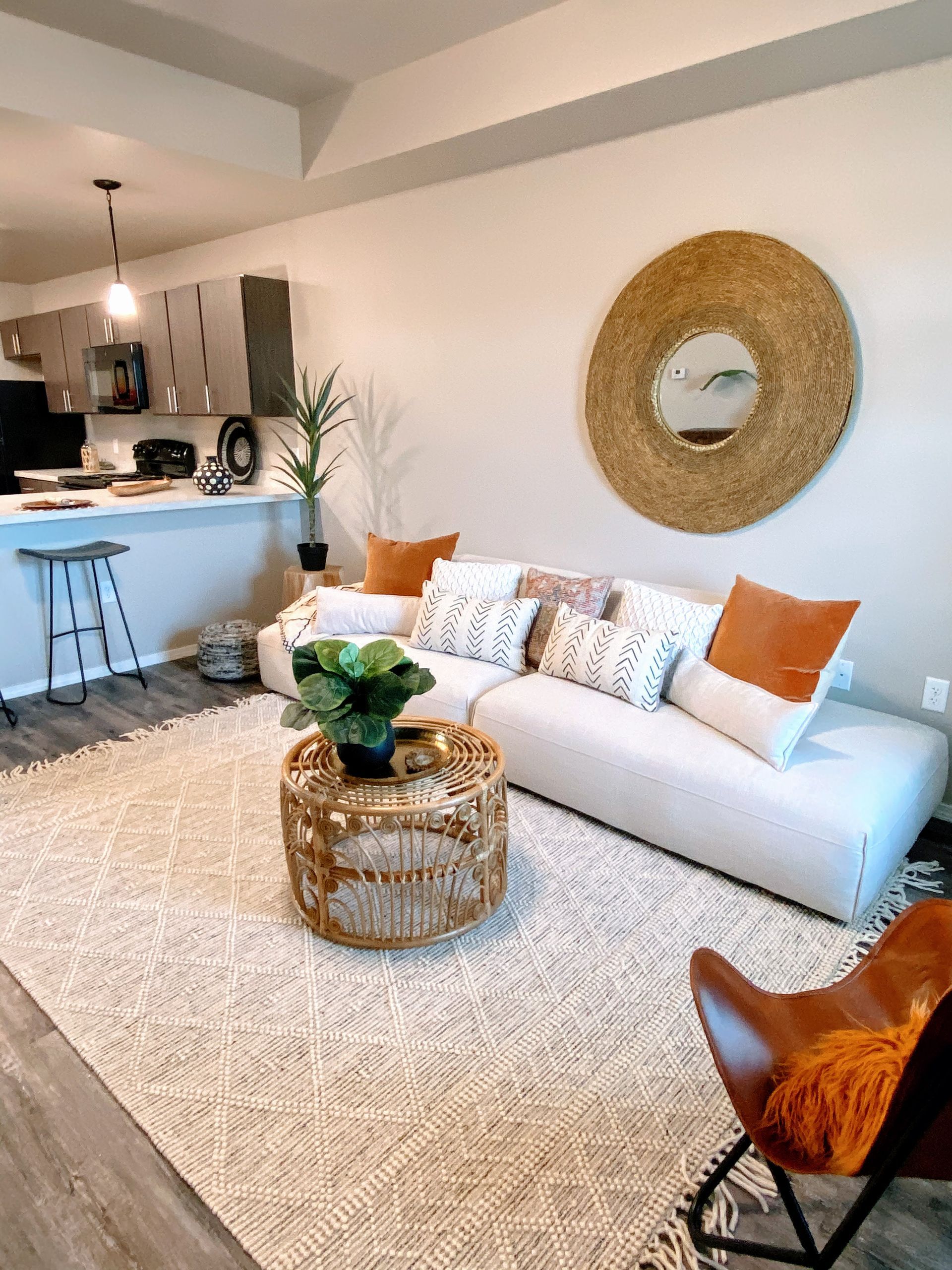 Cozy living room with beige sectional sofa, patterned rug, and round woven mirror.