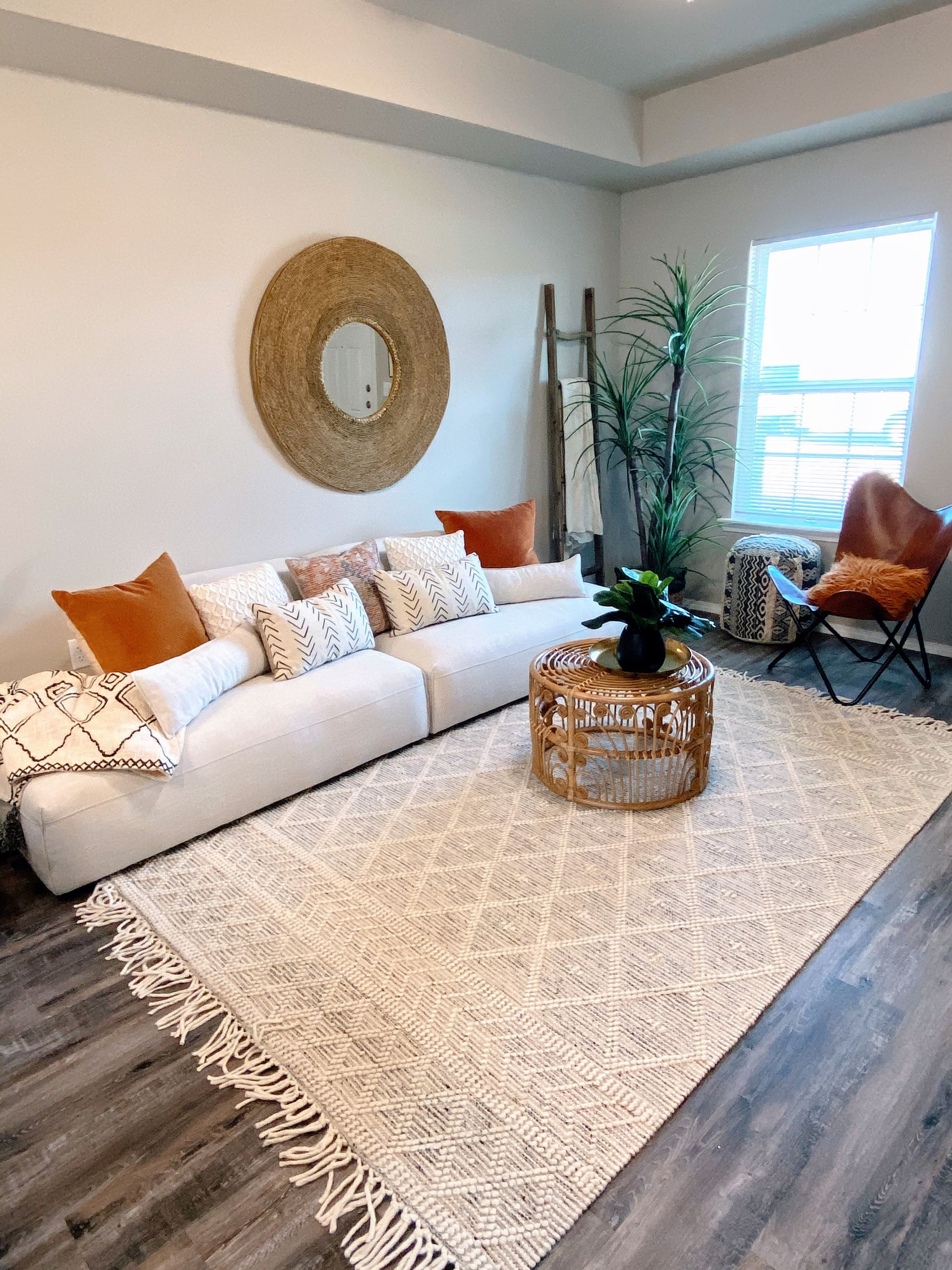 Living room with cream-colored sectional sofa, round mirror, and textured rug. Earth-toned decor.