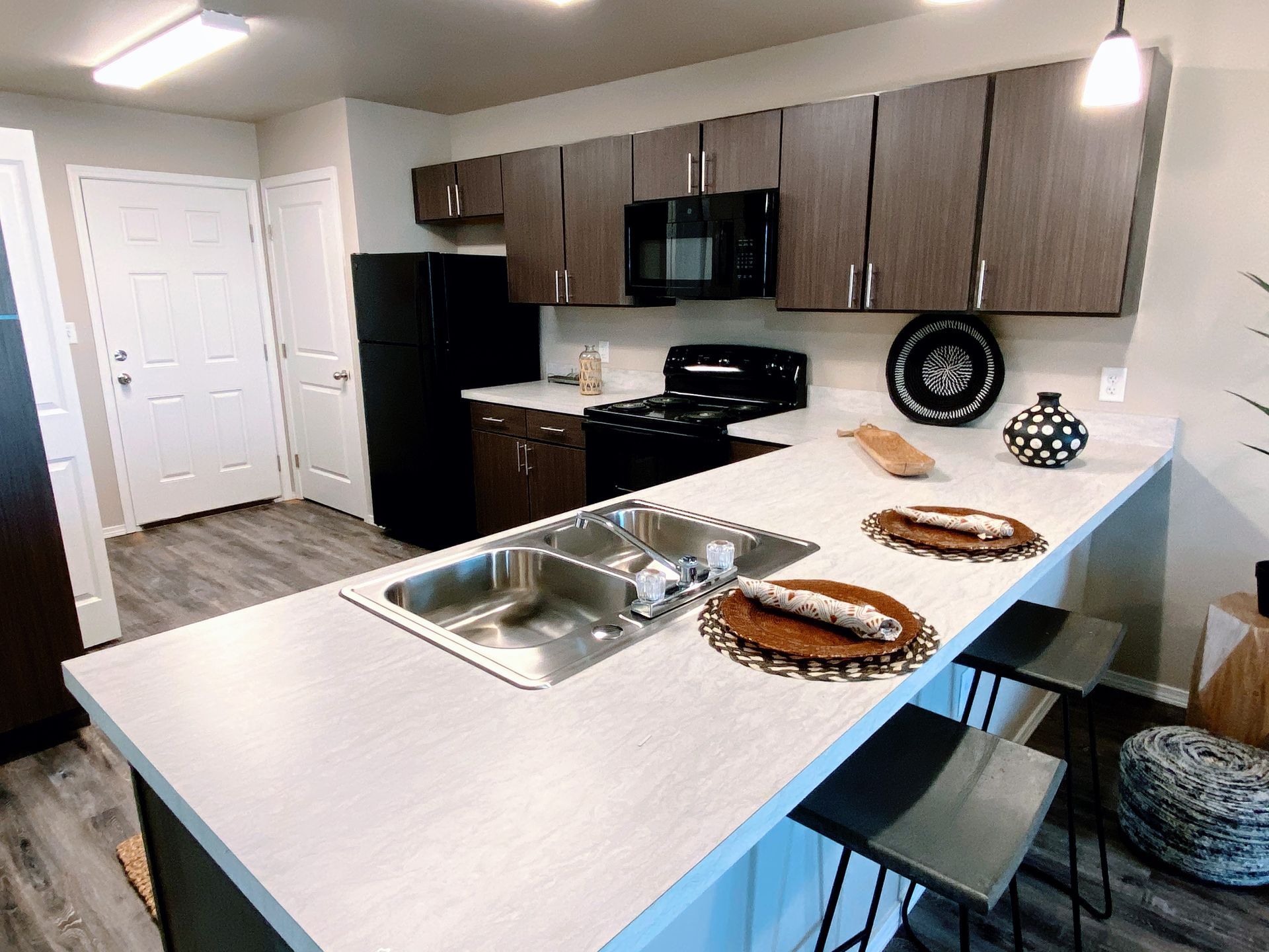 Modern kitchen with brown cabinets, black appliances, and a white countertop with a bar area.