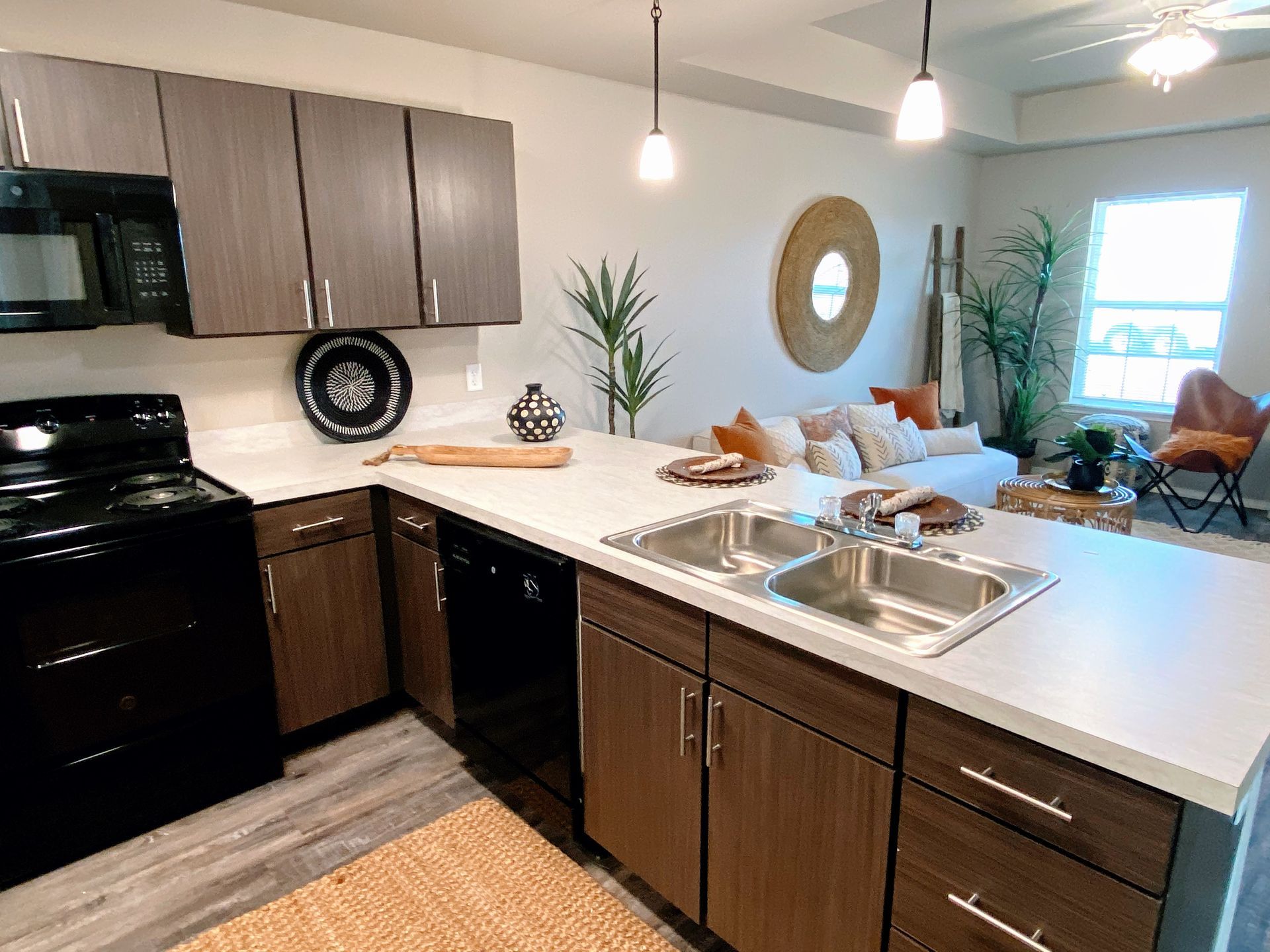 Modern kitchen with island, cabinets, stove, sink, and view into the living room with sofa and plants.
