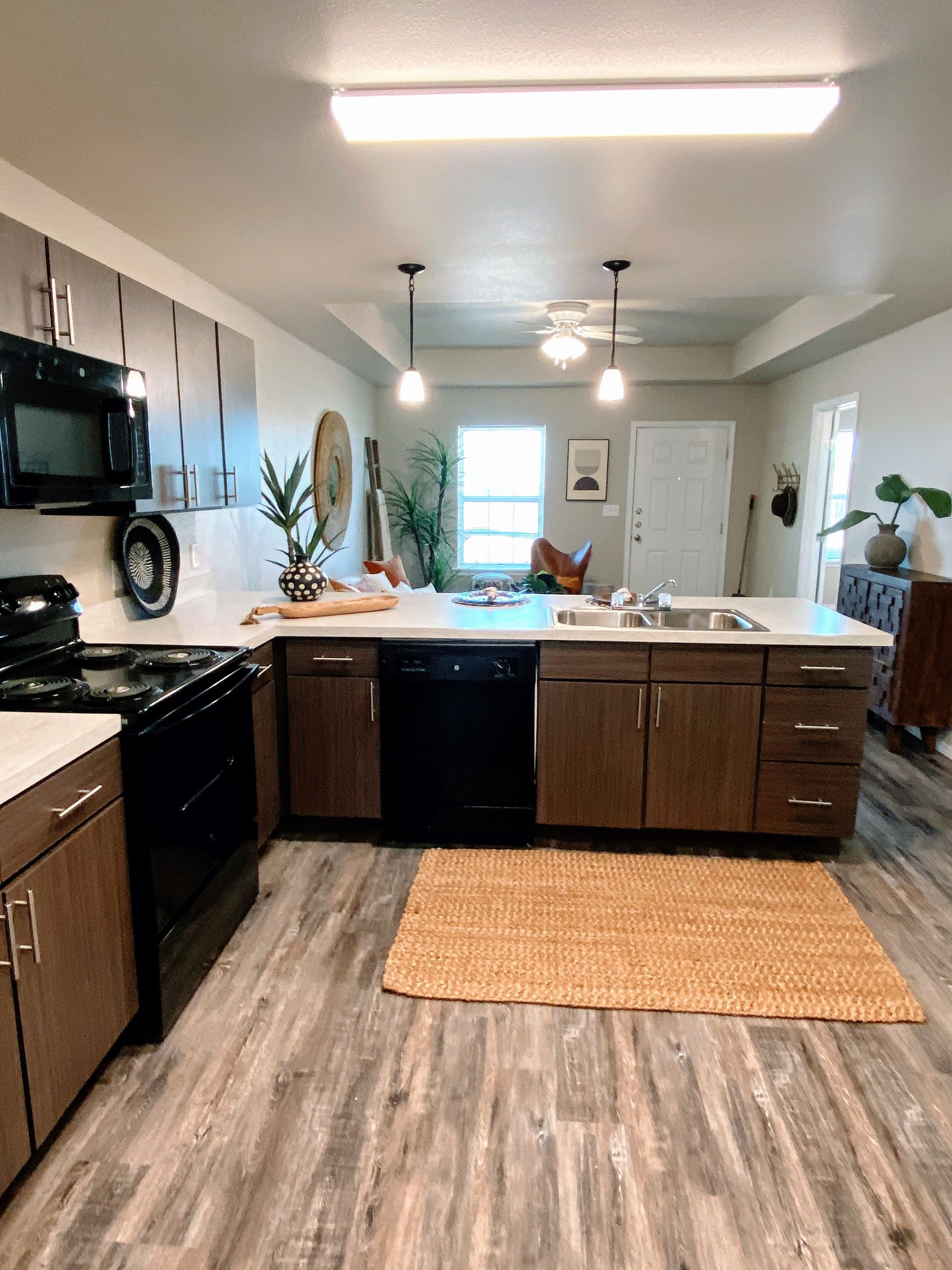 Kitchen with dark brown cabinets, black appliances, and a jute rug.