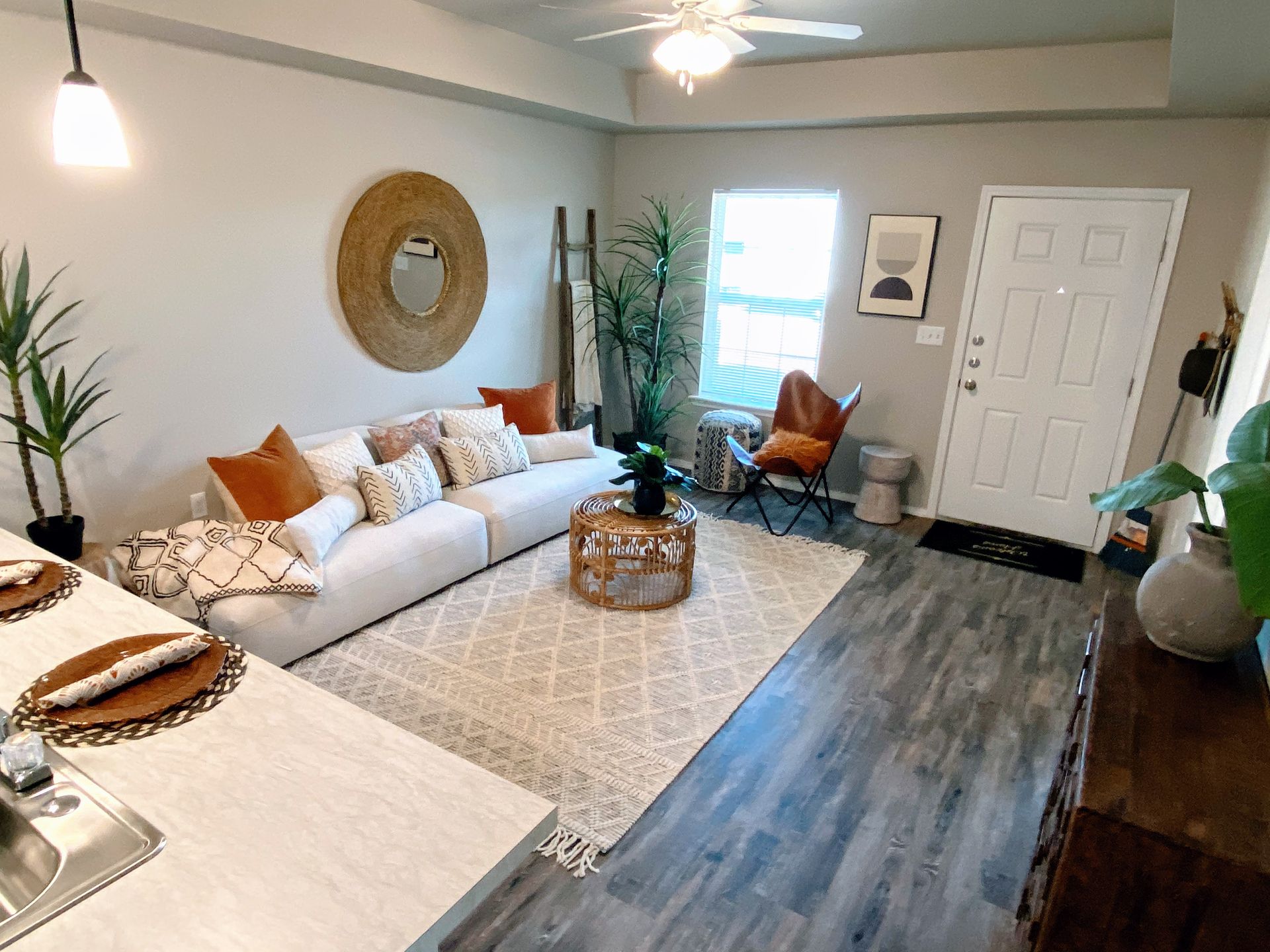 Living room with white sofa, rug, and wooden coffee table; neutral color scheme, plants, door on right.