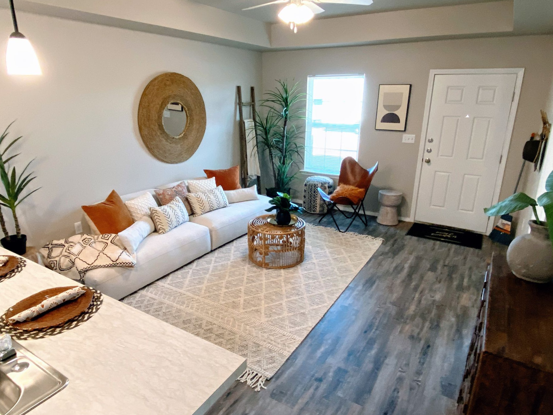 Living room with white sofa, rug, and wooden coffee table; neutral color scheme, plants, door on right.
