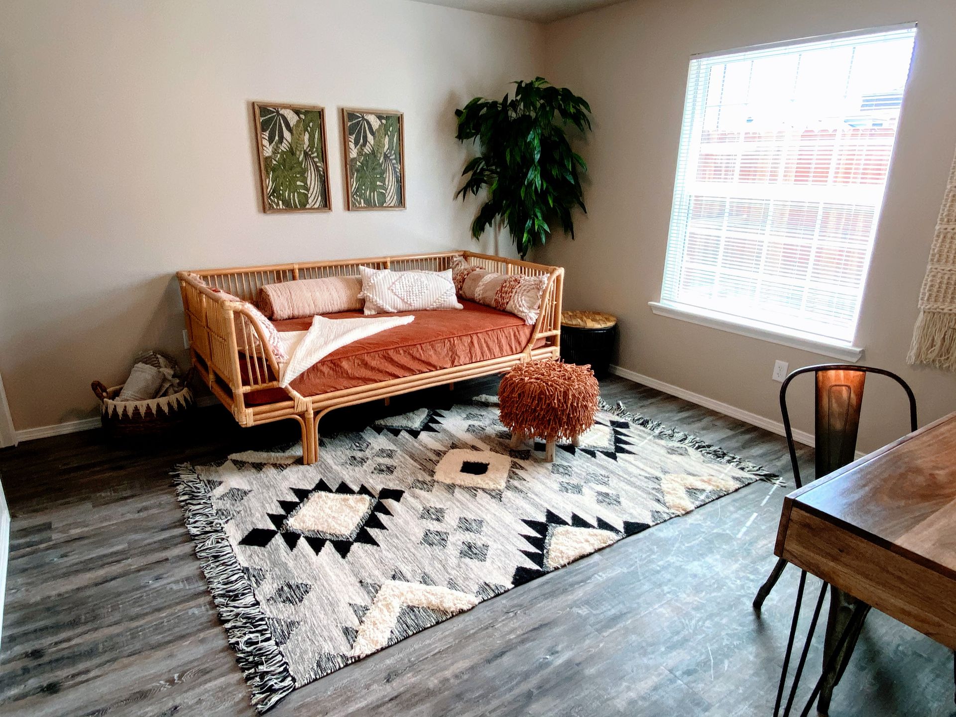Bohemian-style room with daybed, rug, plants, desk, and window.