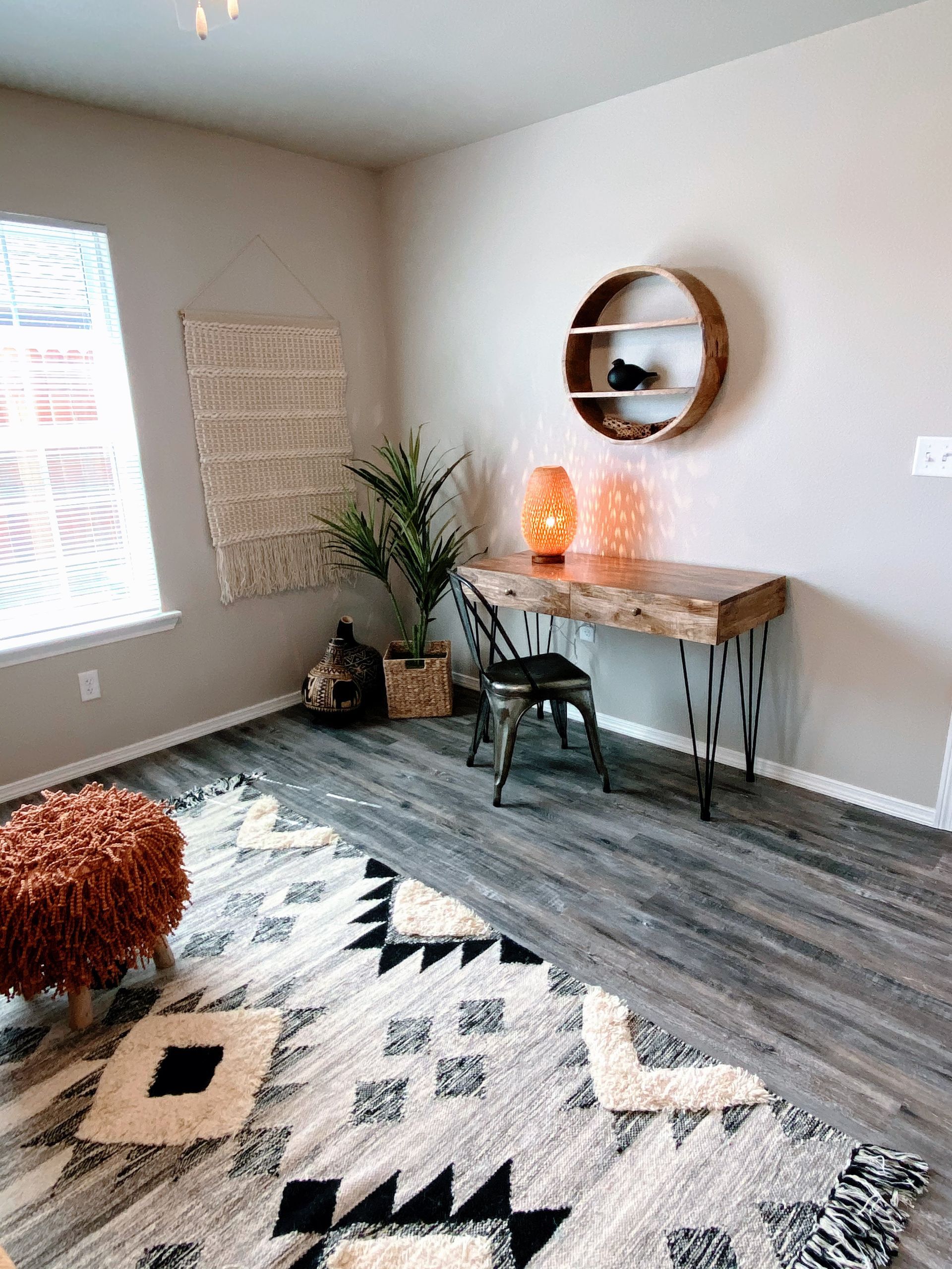 Boho-style room with wooden desk, round shelf, patterned rug, and textured wall hanging.