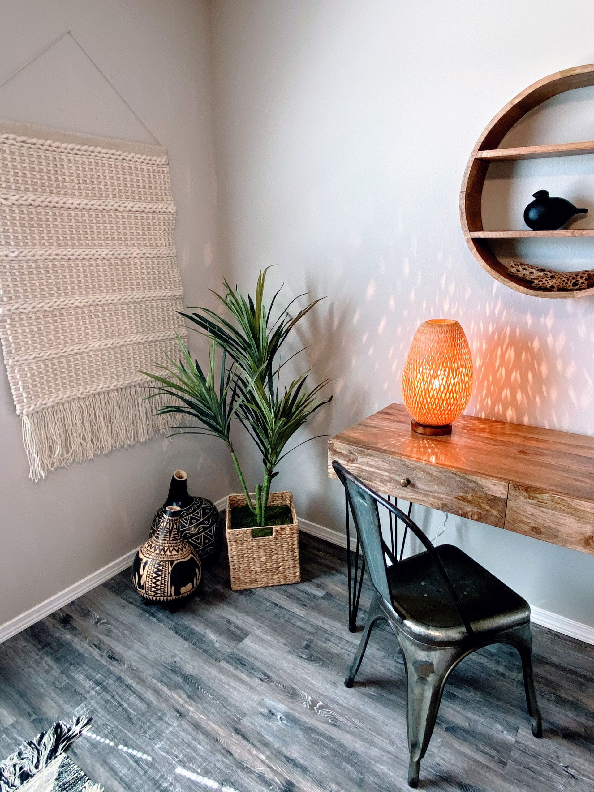 Cozy home office with wood desk, metal chair, woven wall hanging, and decorative lamp.
