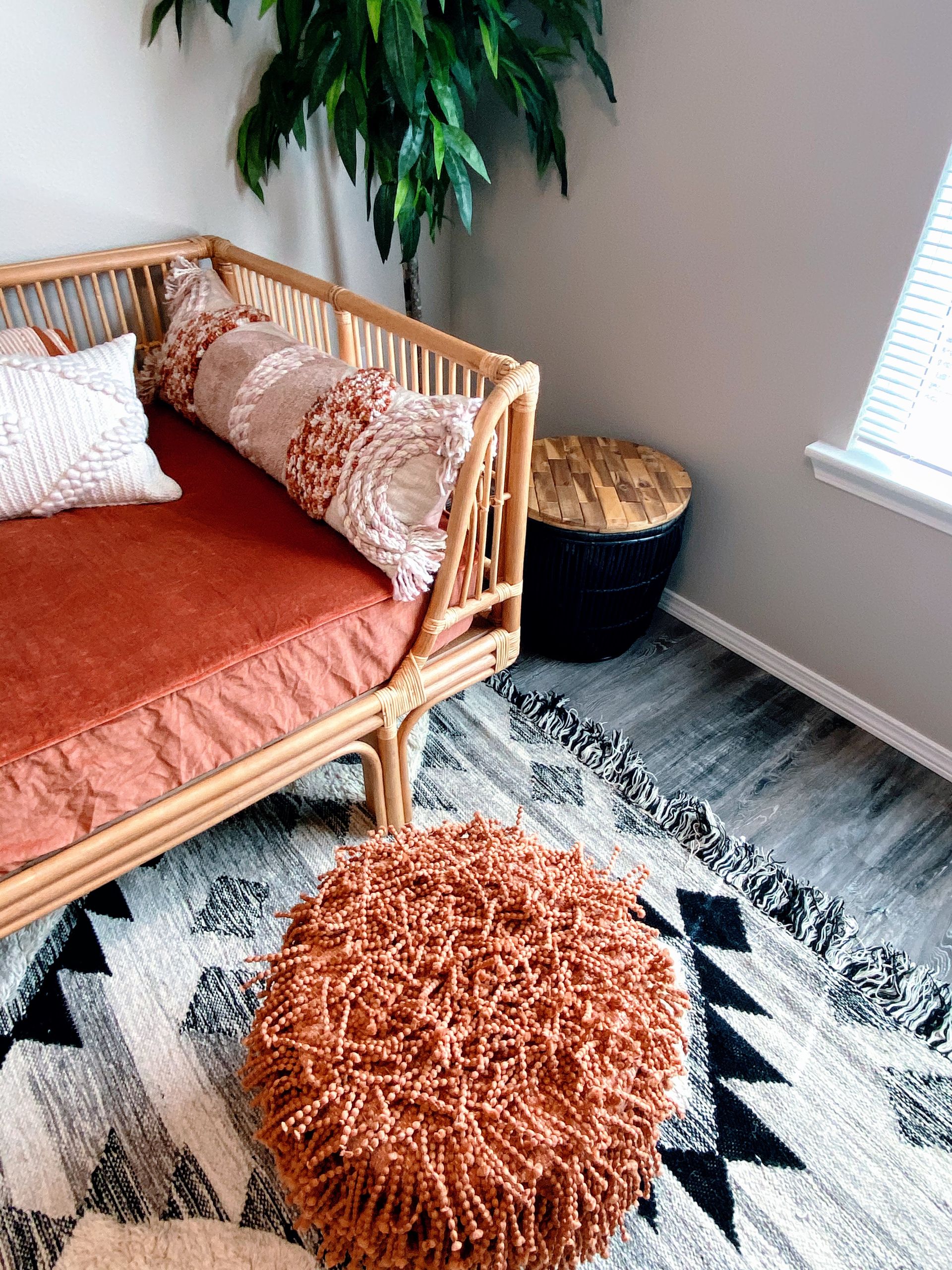 Bohemian-style living room corner with a rattan daybed, terracotta cushions, patterned rug, and a fringed ottoman.