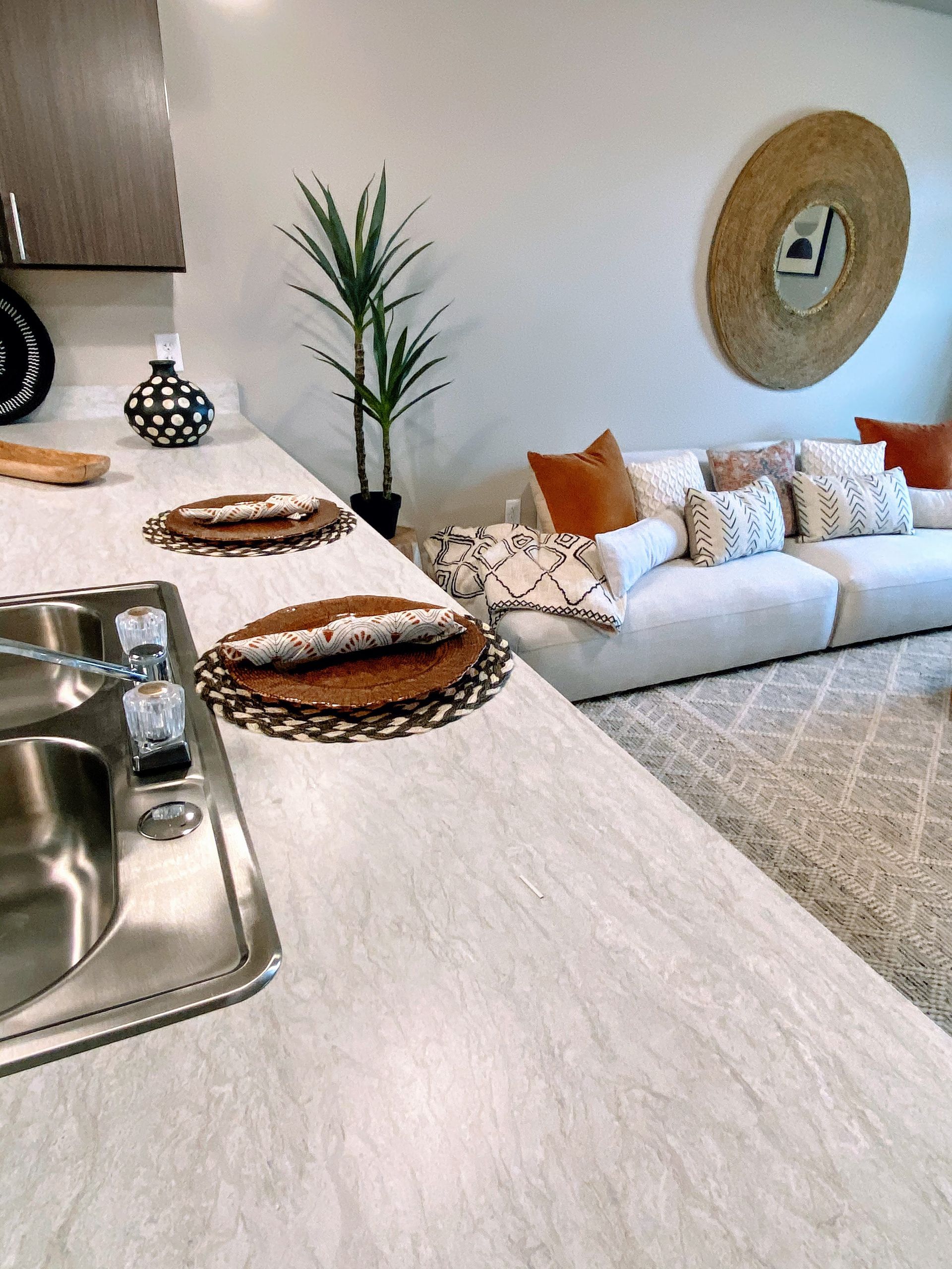 Kitchen with countertop, sink, and plates. Living area with couch, pillows, rug, and mirror on the wall.