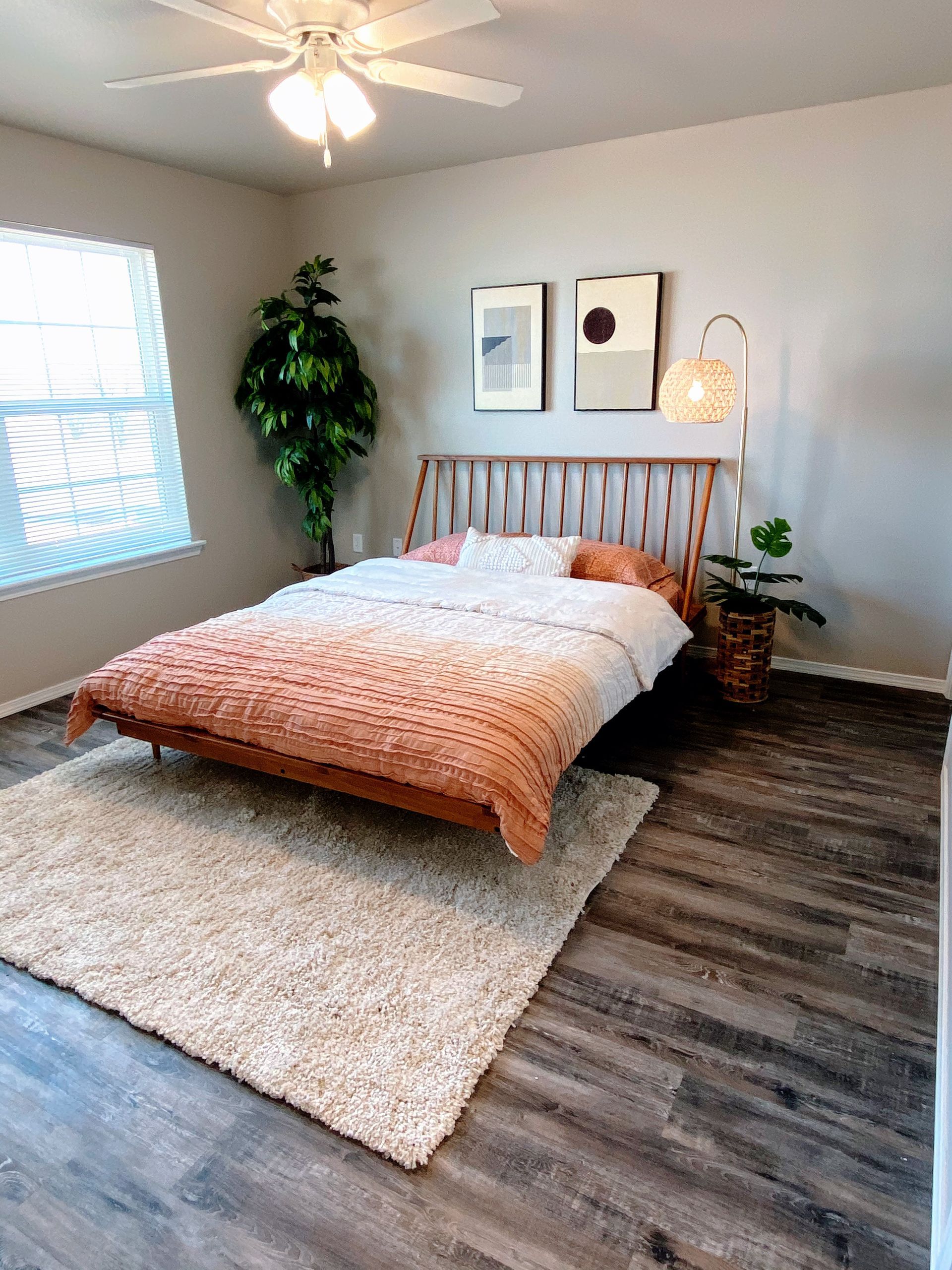 Bedroom with wooden bed, fluffy rug, and plants. Light color scheme.