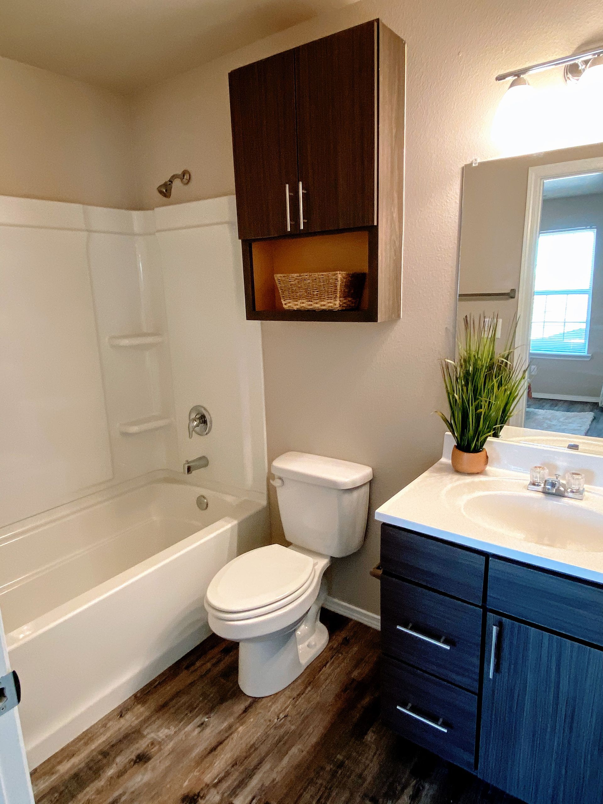 Bathroom with white tub, toilet, dark cabinet, and vanity with plant.