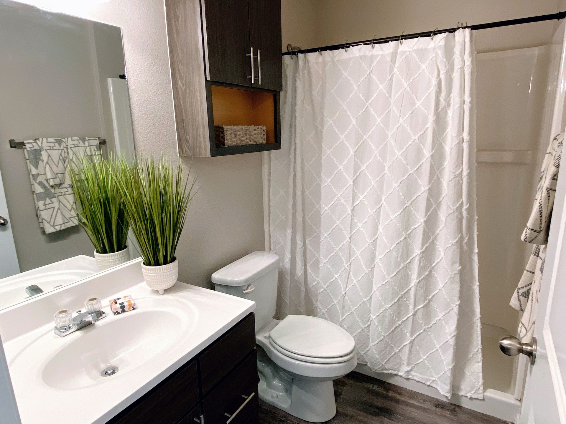 Bathroom with white sink, toilet, and shower curtain. Dark cabinets, gray walls, and faux wood floor.