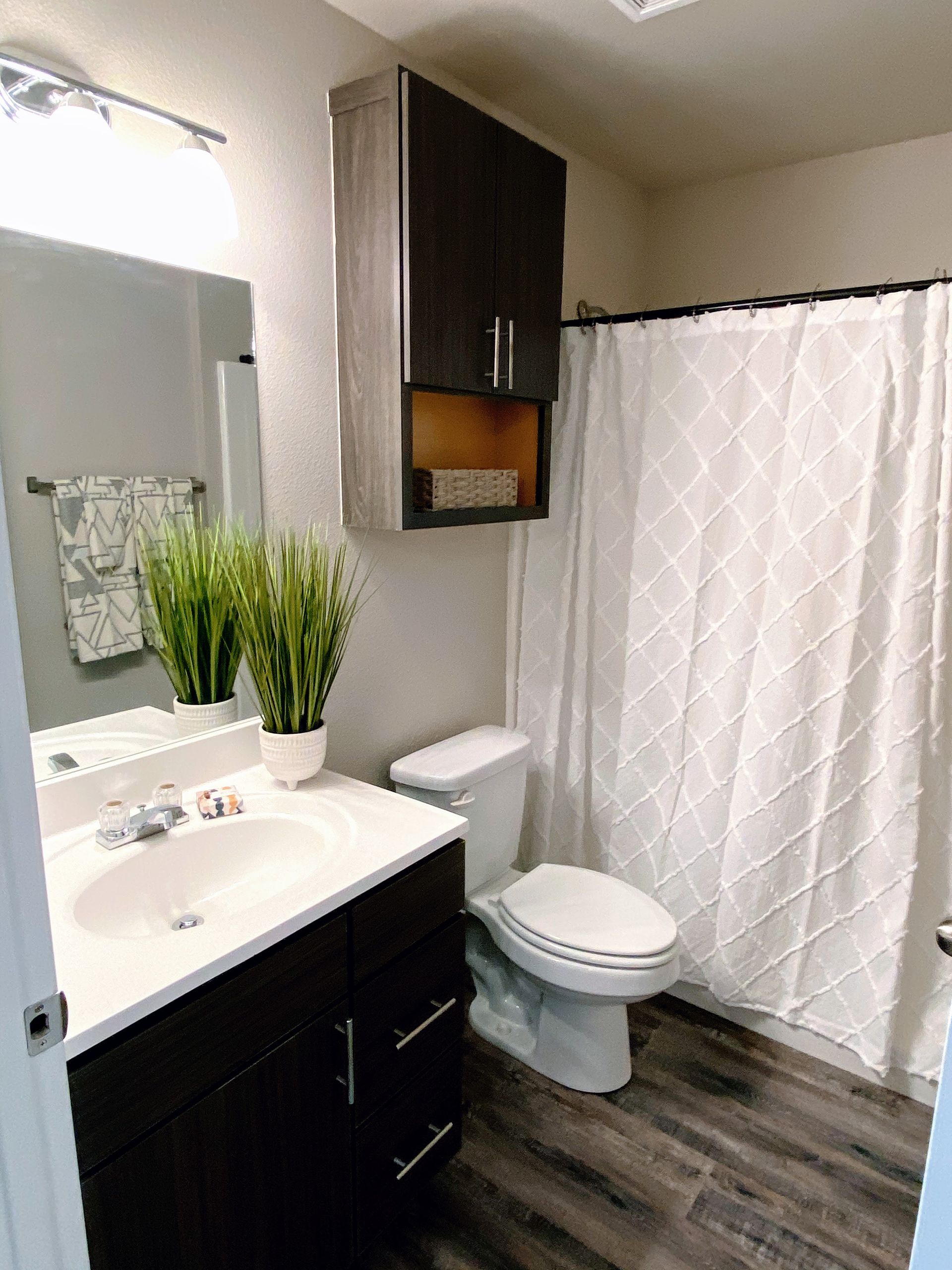 Bathroom with dark cabinets, white countertop and sink, toilet, and patterned shower curtain.