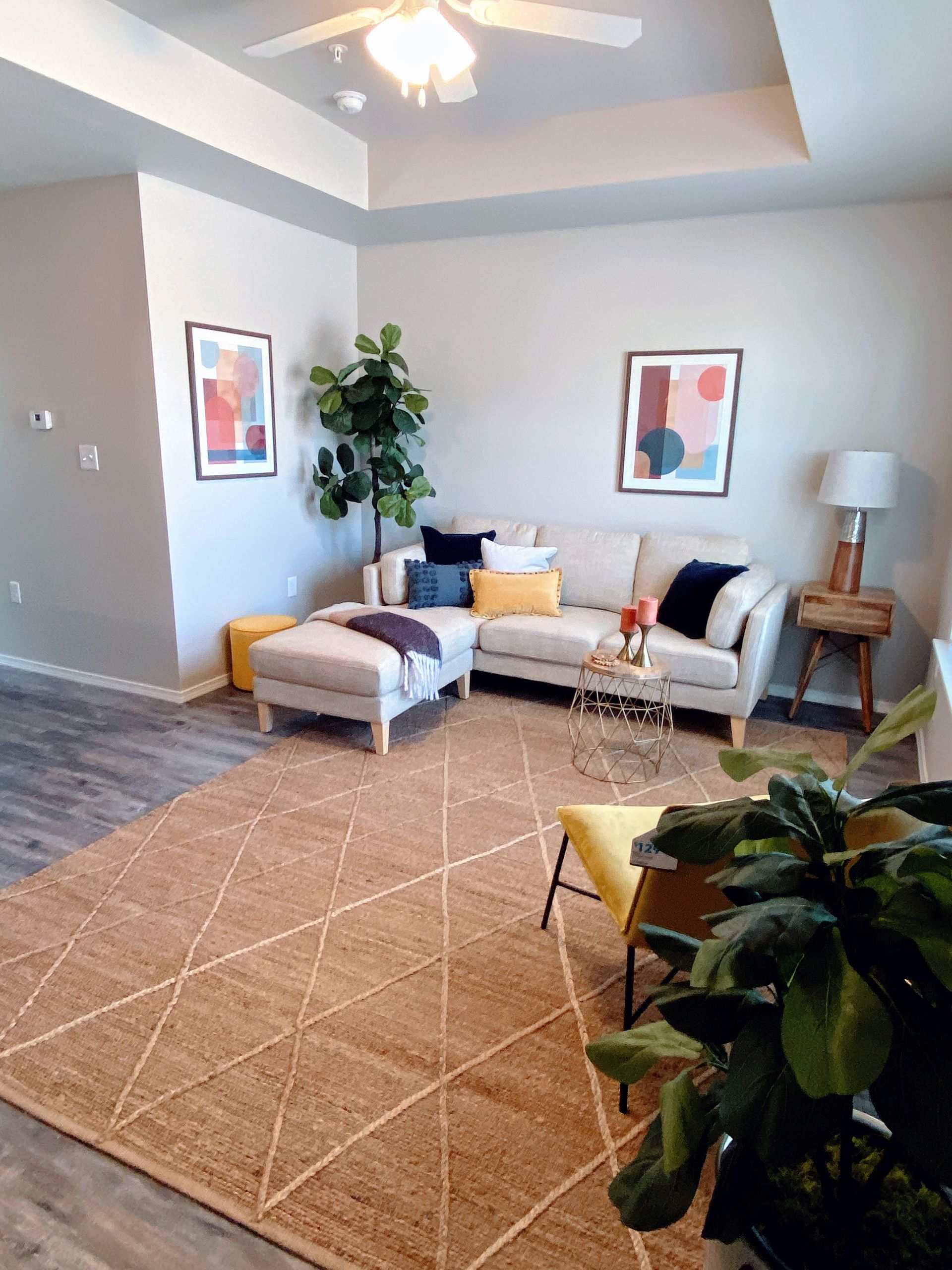 Living room with sectional sofa, rug, artwork, plants, and side table.