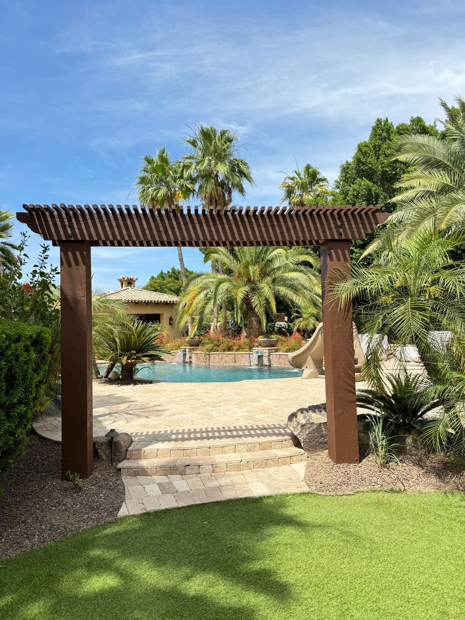 A wooden archway leading to a swimming pool surrounded by palm trees.