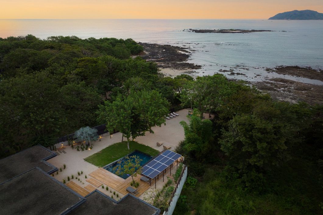 An aerial view of a swimming pool surrounded by trees near the ocean.